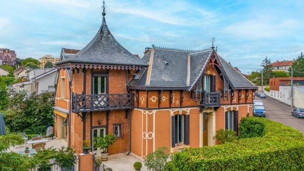 A two-story house with a balcony, a chimney, and a garden.