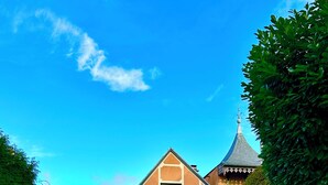 A swimming pool with lounge chairs, a house with a distinctive architectural style, and a clear blue sky.
