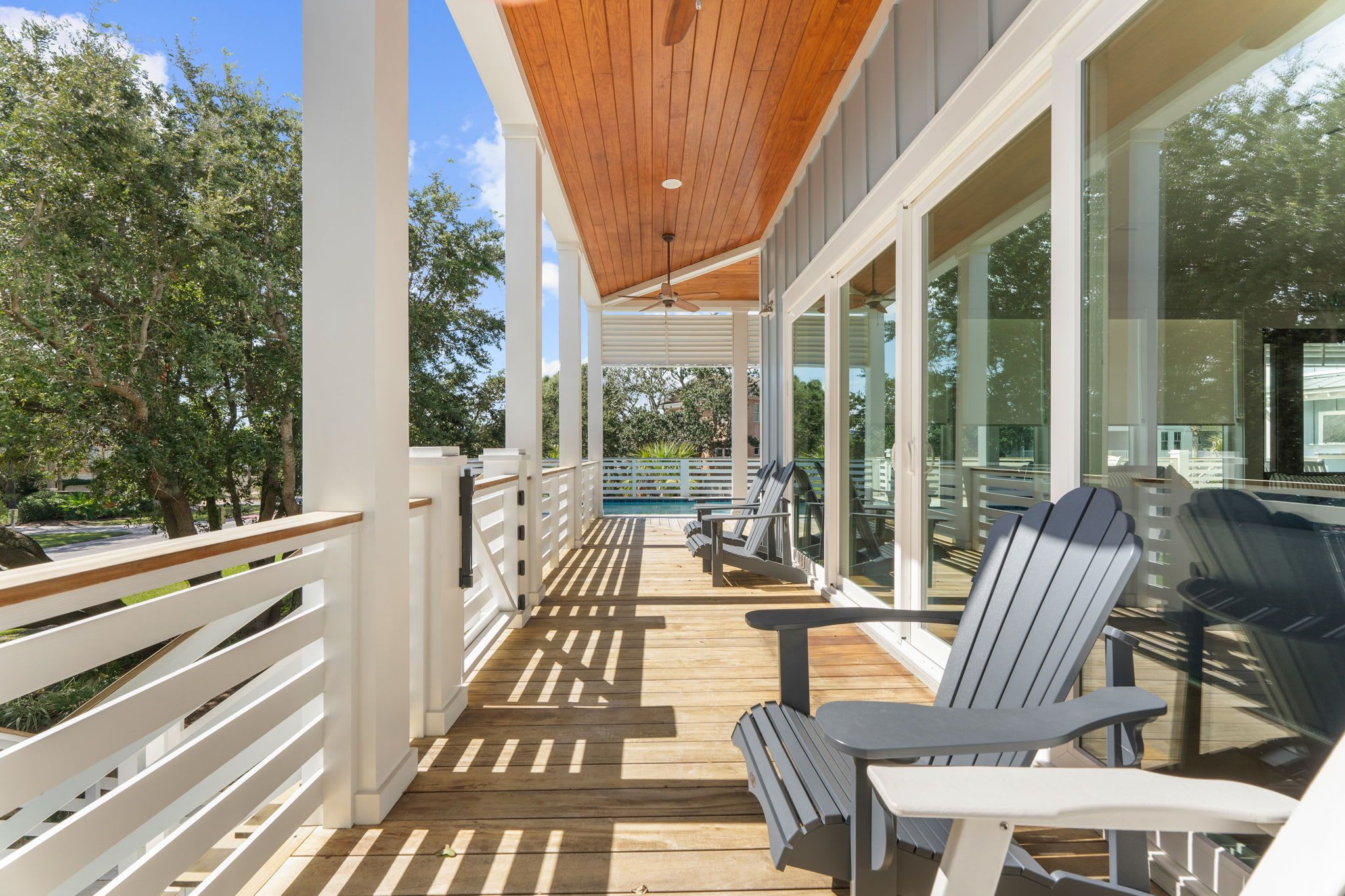 A covered outdoor deck with a wooden ceiling, white railings, and a view of a swimming pool.