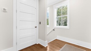 Une pièce avec une porte blanche, une fenêtre donnant sur des arbres et un plancher en bois.