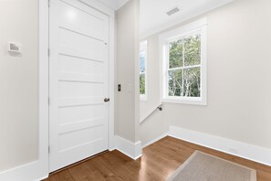 A room with a white door, a window with a view of trees, and a wooden floor.