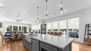 Une cuisine moderne dotée d’un grand îlot central, de planchers en bois et offrant une vue sur l’extérieur grâce à de grandes fenêtres.