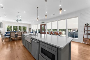A modern kitchen with a large island, wooden flooring, and a view of the outdoors through large windows.