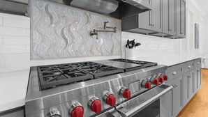 Une cuisine dotée d’une hotte en acier inoxydable, d’un dosseret carrelé et d’une cuisinière à gaz avec des boutons rouges.