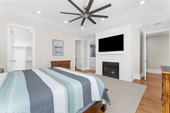 A bedroom with a bed, a television, a fireplace, and a ceiling fan.