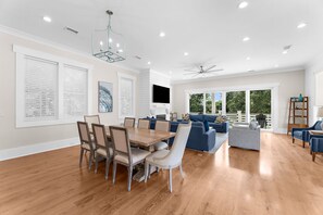 A spacious living room with a dining area, large windows, and a ceiling fan. - Luxurious 6 Bedroom House Across From Beach! (Isle of Palms)