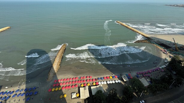 A beach with a long stretch of umbrellas and beach chairs, a sandy shore, and waves crashing onto the beach. - Apartamentos Palmetto Eliptic ICDI (Cartagena)