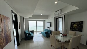 A modern living room with a glass door leading to a balcony, a dining area with a glass table, and a large painting on the wall. - Apartamentos Palmetto Eliptic ICDI (Cartagena)