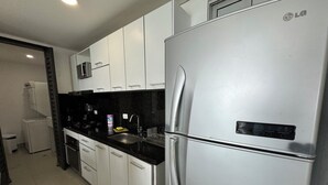 A modern kitchen with white cabinets, a stainless steel refrigerator, and a black countertop. - Apartamentos Palmetto Eliptic ICDI (Cartagena)