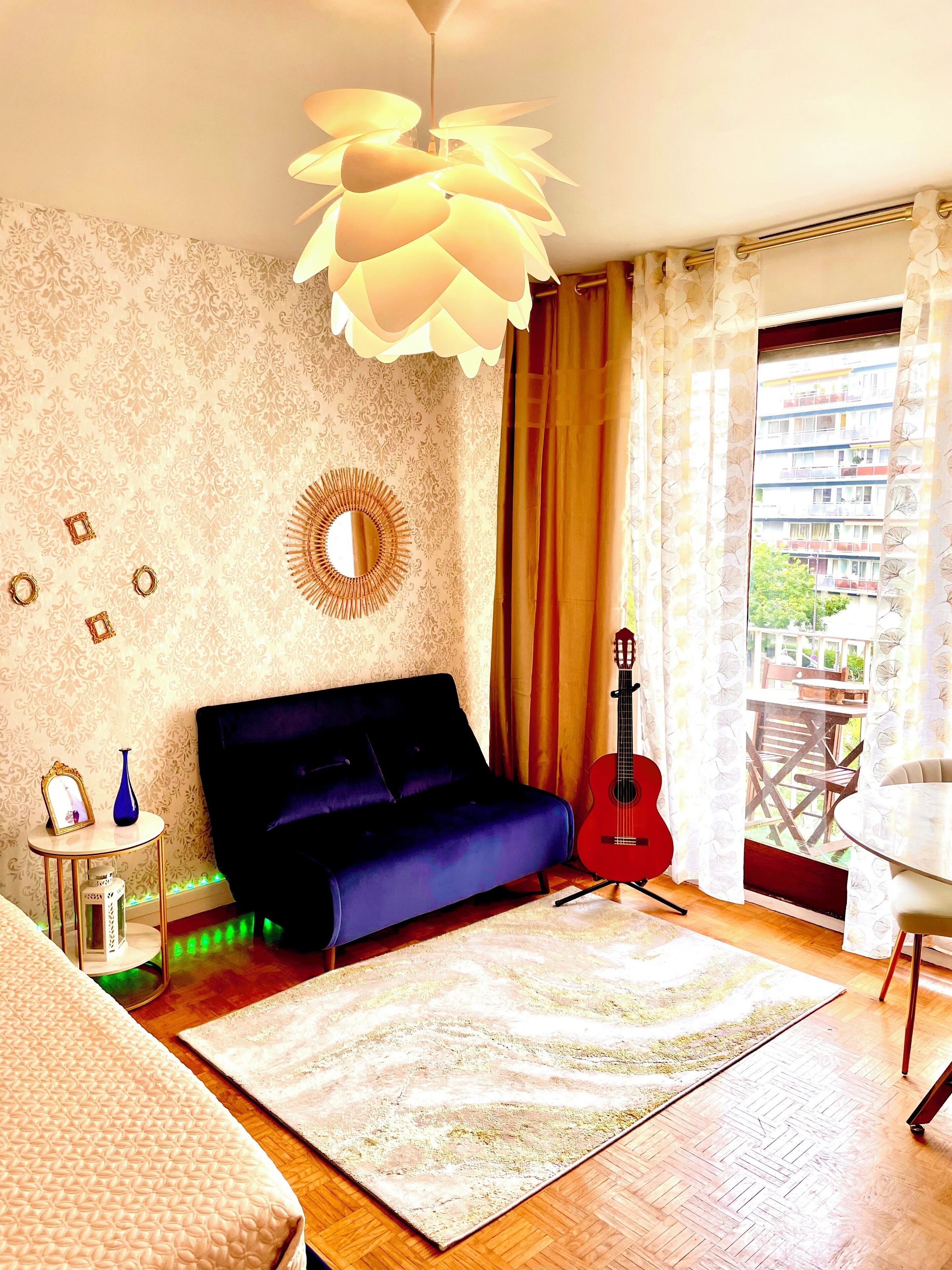 Une pièce avec un canapé bleu, une guitare rouge, un miroir rond et un tapis à motifs.