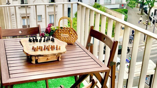 A wooden table with a chessboard, chairs, a wicker basket, and a lantern on a balcony with a view of buildings and a street. - Paris appartment Eiffel Tour (Paris)