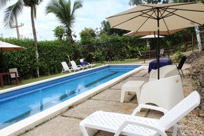 A swimming pool with lounge chairs and umbrellas, surrounded by greenery. - Hotel vista Bonita- Tucan Room (Parrita)