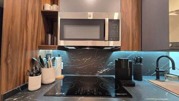 A kitchen with a built-in microwave, a stovetop, and a marble backsplash.