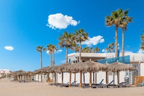 Una playa con palmeras, sillas de playa y sombrillas de paja.