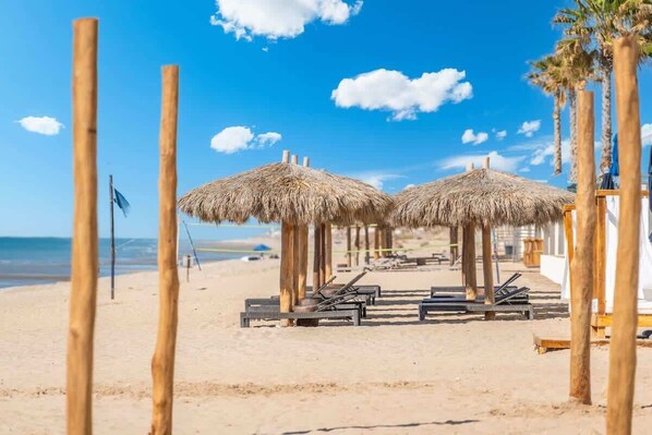 A beach with thatched umbrellas and sun loungers.