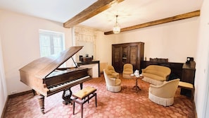 Un piano à queue dans un salon, avec un sol carrelé, un meuble en bois et deux fauteuils.