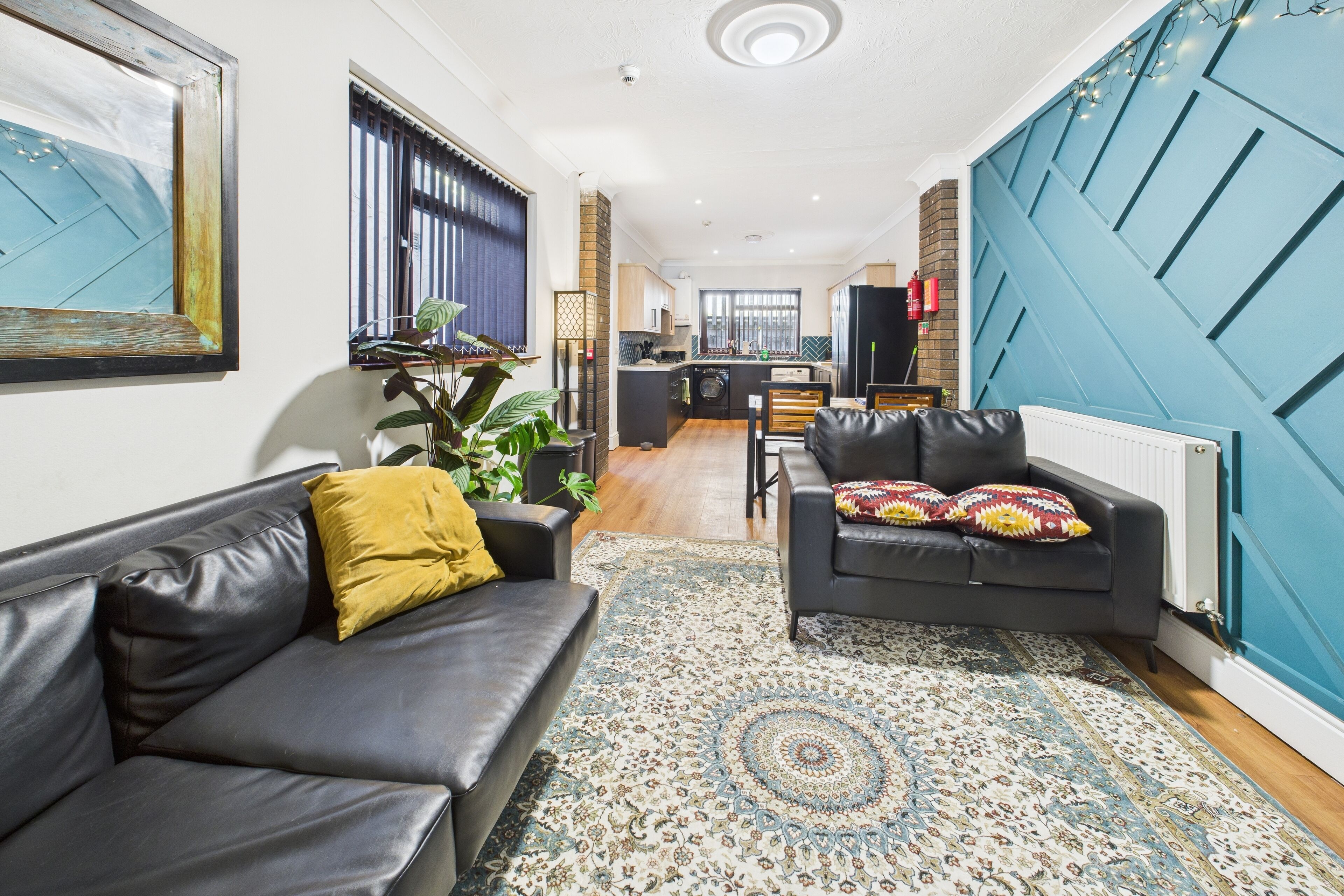 A modern living room with a black leather sofa, a patterned rug, and a blue accent wall.
