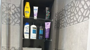 Un baño con artículos de aseo en estantes, incluyendo una botella amarilla, un tubo blanco y una botella morada.