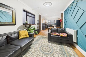 A modern living room with a sofa, a coffee table, and a patterned rug. There is a kitchen area in the background with a dining table and chairs. - The Phoenix (Swansea)