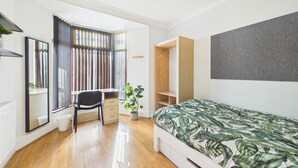 Un dormitorio con cama, escritorio, silla, armario y ventana con cortinas.