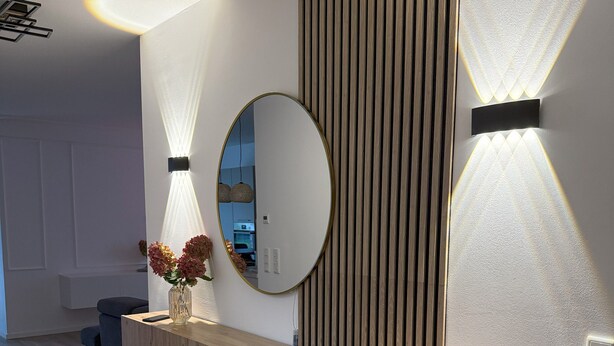 Een modern interieur met een houten console tafel, een grote spiegel en twee wandlampen.