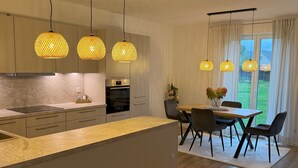 Een moderne keuken met een centraal eiland, hangende lampen en een eethoek met een tafel en stoelen.