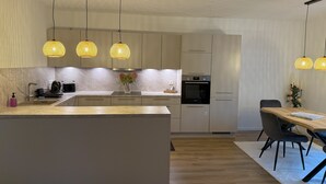 Een moderne keuken met een centraal eiland, hanglampen en een eethoek met een tafel en stoelen.