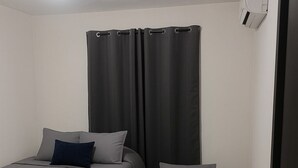 Ein Zimmer mit zwei Betten, einem Vorhang, einer Tür und einer Klimaanlage.
