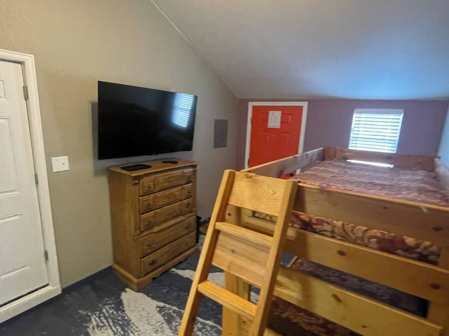 A room with a bunk bed, a TV, a wooden dresser, and a door with a red frame.