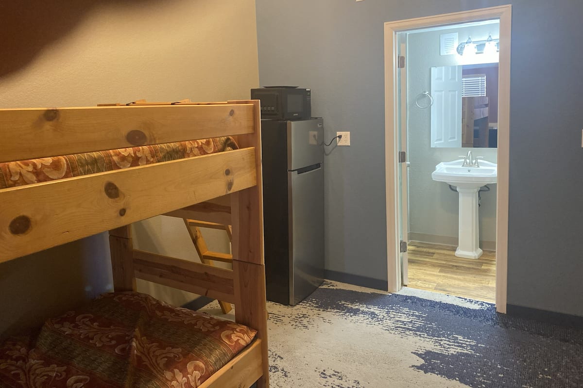 A room with a bunk bed, a refrigerator, and a bathroom visible through an open door.