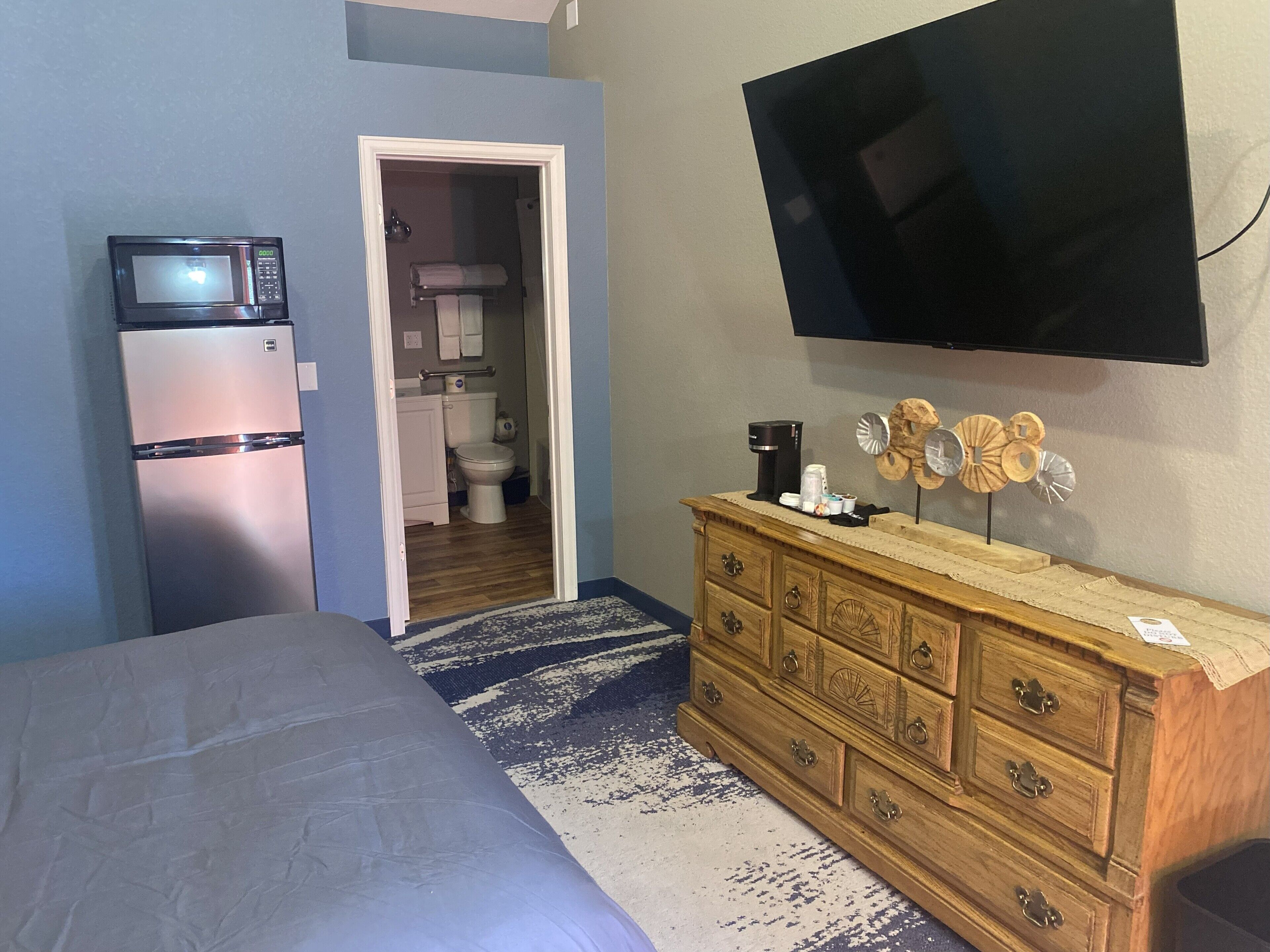 A bedroom with a bed, a dresser, a television, a microwave, and a bathroom visible through an open door.