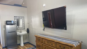 Cozinha compacta com geladeira, pia, micro-ondas e um armário de madeira com gavetas.