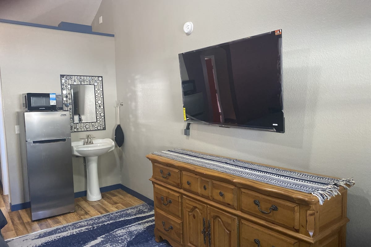 A compact kitchen with a refrigerator, sink, microwave, and a wooden cabinet with drawers.