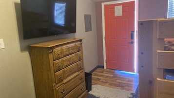 A hallway with a wooden dresser, a flat-screen TV mounted on the wall, a red door, and a patterned rug on the floor.