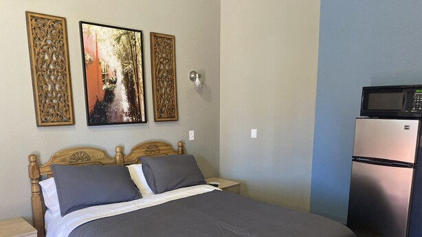 Quarto com cama, mesa de cabeceira, frigorífico e arte decorativa na parede.