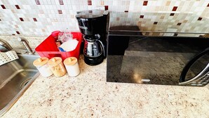 Uma cozinha com pia de aço inoxidável, cafeteira e micro-ondas. Há potes com tampas e uma cesta vermelha com objetos.