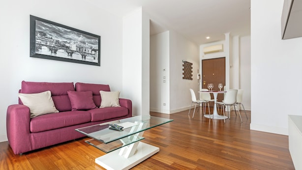 A modern living room with a glass coffee table, a purple sofa, and a dining area with white chairs and a table. - 15 Minutes Walk From Vatican Museums (Roma)