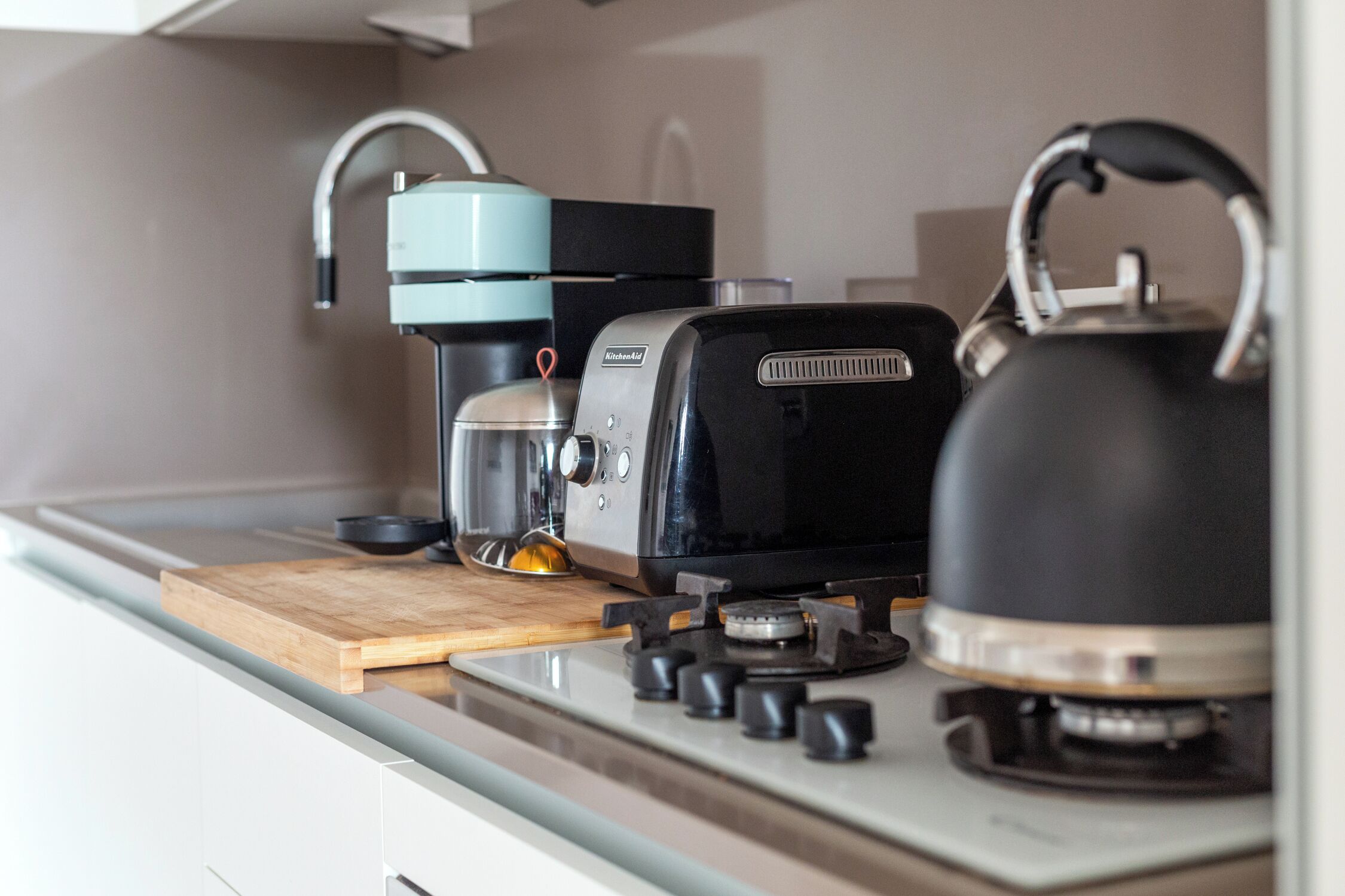 A kitchen with a coffee maker, kettle, and a cutting board on the counter.