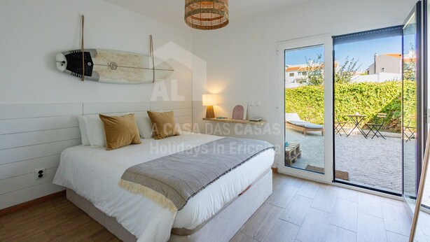 Ein Schlafzimmer mit einem Bett, einer Hängelampe und einer Glastür, die zu einem Außenbereich mit Tisch und Stühlen führt.