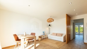 Ein geräumiger Wohnbereich mit einem Holzessttisch, zwei Stühlen, einem weißen Sofa und einer Pendelleuchte.