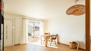 Ein geräumiges Zimmer mit einem Holzespeisetisch, Stühlen, einer Weidenkorb-Pendelleuchte und Blick durch eine Glastür auf einen Außenbereich.