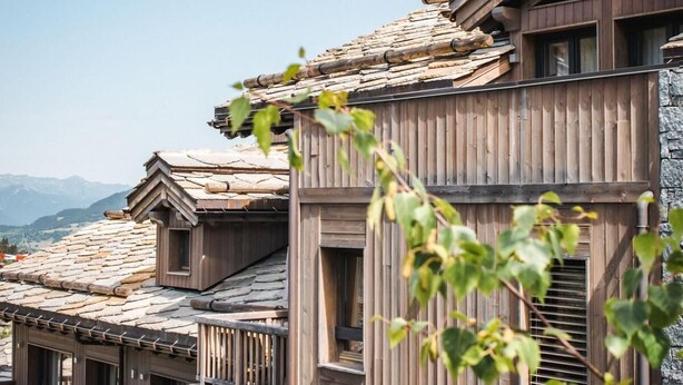Una tradicional cabaña de madera con techo inclinado, balcones de madera y base de piedra.
