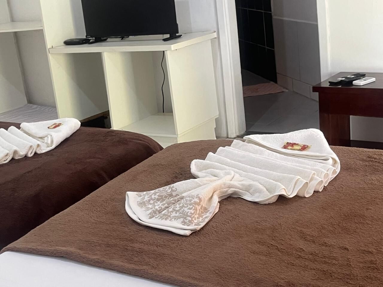 Ein Raum mit zwei Massagetischen, die mit Handtüchern abgedeckt sind, einem Fernseher auf einem Schrank und einem Schreibtisch mit Computer und Telefon.