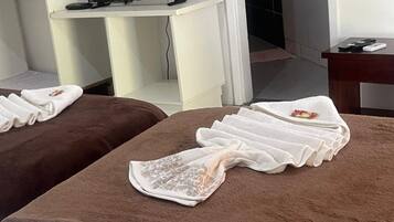 Ein Raum mit zwei Massagetischen, die mit Handtüchern abgedeckt sind, einem Fernseher auf einem Schrank und einem Schreibtisch mit Computer und Telefon.