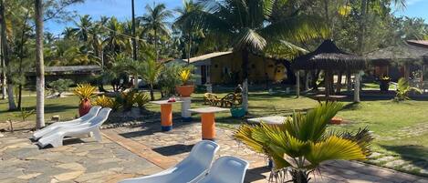 A resort area with lounge chairs, palm trees, and a thatched-roof structure.