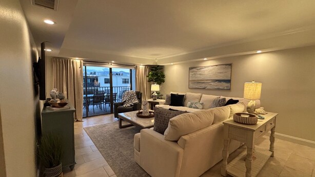 A spacious living room with a sofa, coffee table, and a lamp. There is a sliding glass door leading to a balcony. - Spacious Top-Floor Condo w/beach access & Intracoastal Views (Indian Shores)