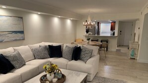A modern living room with a sectional sofa, a marble coffee table, and a dining area with a chandelier. - Spacious Top-Floor Condo w/beach access & Intracoastal Views (Indian Shores)