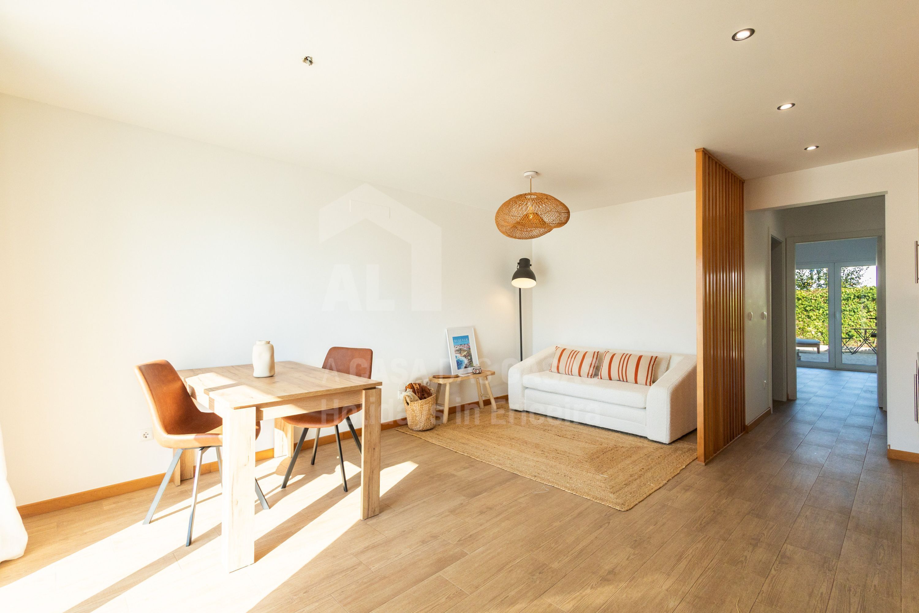 Ein großzügiger Wohnbereich mit einem Holzesstisch, einem weißen Sofa und einem großen Fenster, das für natürliches Licht sorgt.