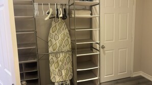 Un dressing avec de nombreuses étagères et un espace pour suspendre les vêtements, une porte et une planche à repasser à motifs.