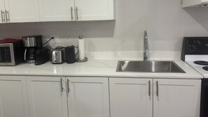 Une cuisine moderne avec des meubles blancs, un évier en acier inoxydable, une machine à café, un grille-pain et une cuisinière.